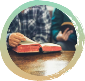 Two individuals sitting next to each other in front of an open Bible on a wooden table.