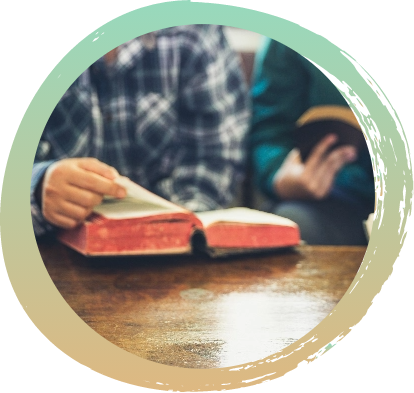 Two individuals sitting next to each other in front of an open Bible on a wooden table.