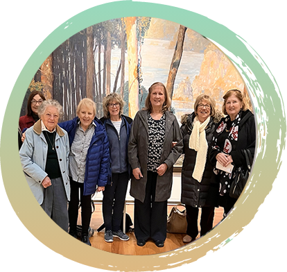 Seven Women from the Advent Women's Circle posing for a picture in front of a wall mural depicting a forrest and lake.