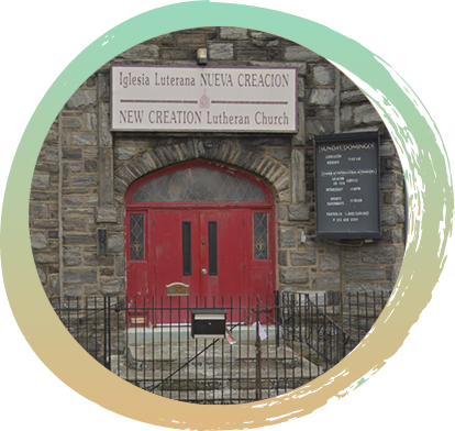 The front of a church that is made of stone, with two large red doors, and a black picket fence around it. The sign over the church door reads "Iglesia Luterana Neuva Creacion New Creation Lutheran Church"