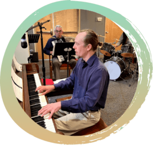 One man is playing the piano in the foreground. In the background there is another man playing the accordion and a third man playing the drums.