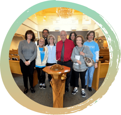 Several individuals, who are volunteers from the Warminster Food Bank, are gathered in the church, in front of the baptismal font.